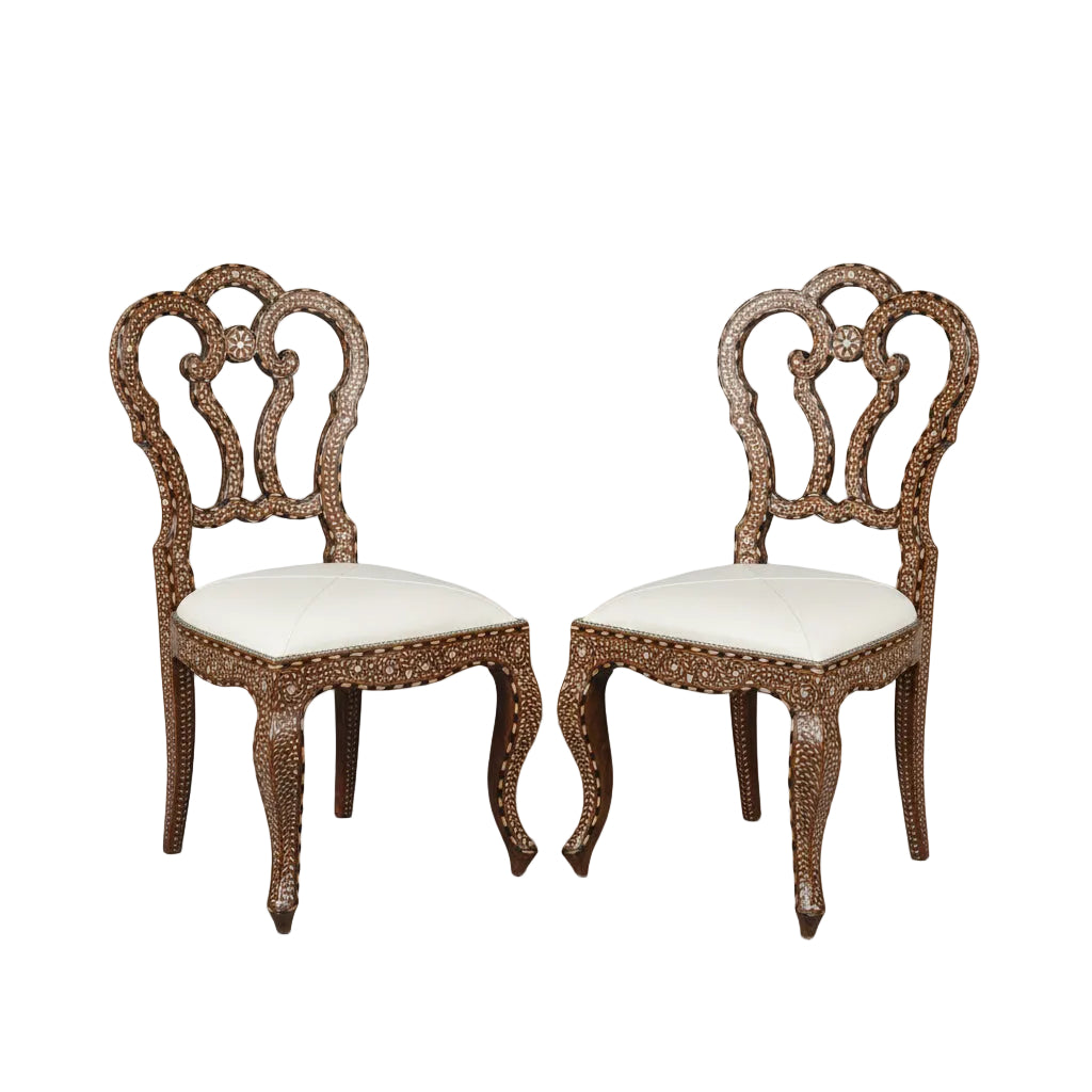 Pair of ornate Anglo Indian chairs with bone inlay and white cushions .