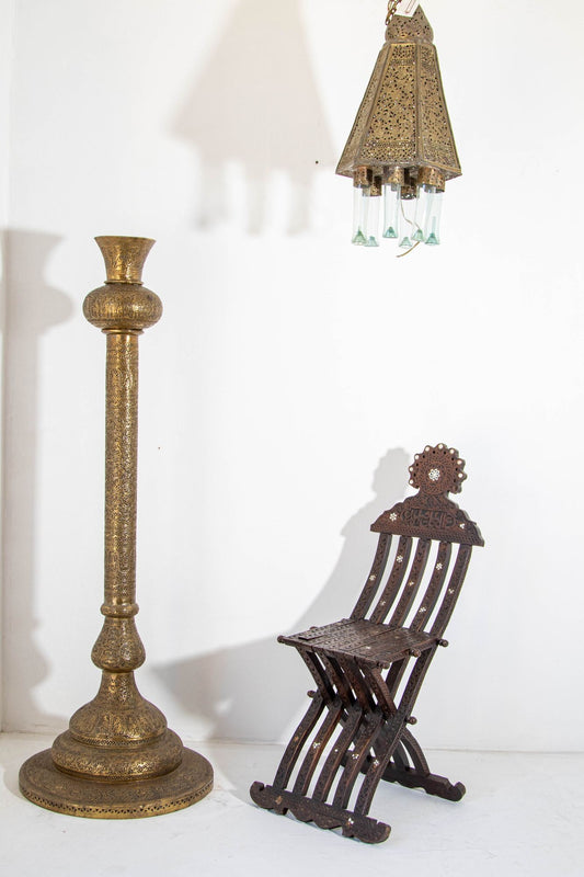 An antique 19th century brass Islamic floor lamp with Kufic Mamluke revival pierced foliate open work, featuring Persian calligraphy and figures, alongside a chair with a similar design.