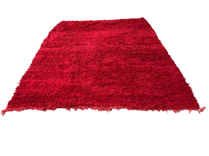 A vintage red fluffy rug with a geometric pattern, known as a Bed of Roses, displayed on a concrete surface.