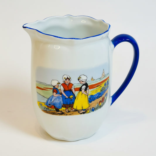Ceramic pitcher with blue rim and handle, featuring a scenic design on a white background