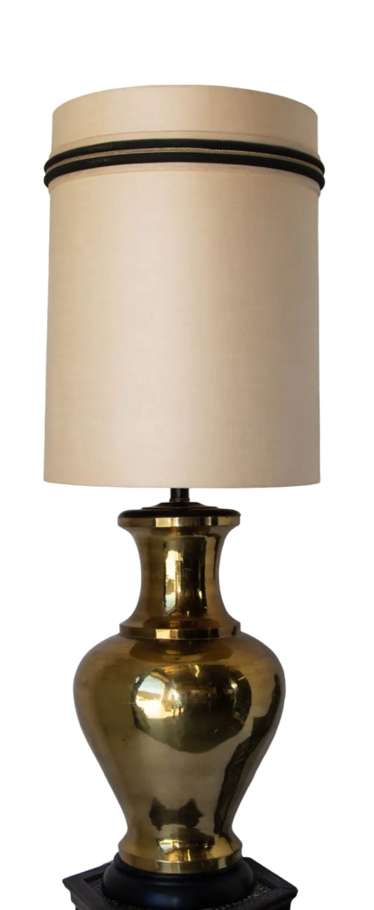 A vintage Hollywood Regency style polished brass urn table lamp with a black lacquered base and shade, featuring a large scale design and artfully spun brass body.