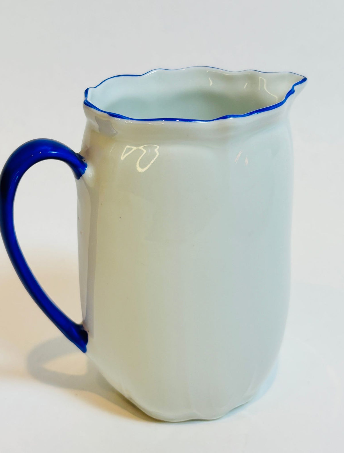 White pitcher with blue rim and handle on a white background