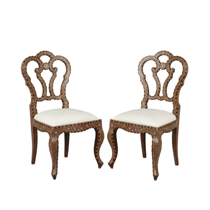 Pair of ornate Anglo Indian chairs with bone inlay and white cushions .