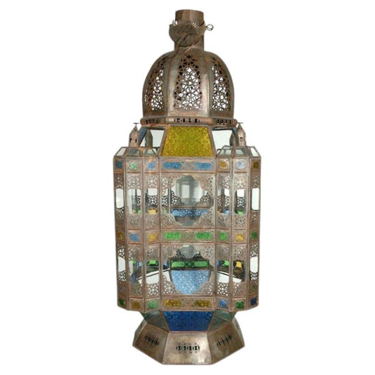 An ornate Moroccan-style metal lantern with intricate cutout patterns and colorful stained glass panels in blue, green, yellow, and white, set against a plain white background.