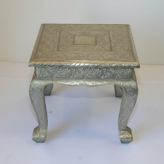A vintage Anglo-Indian silver metal clad square side low table with intricate repousse work and a wooden base.