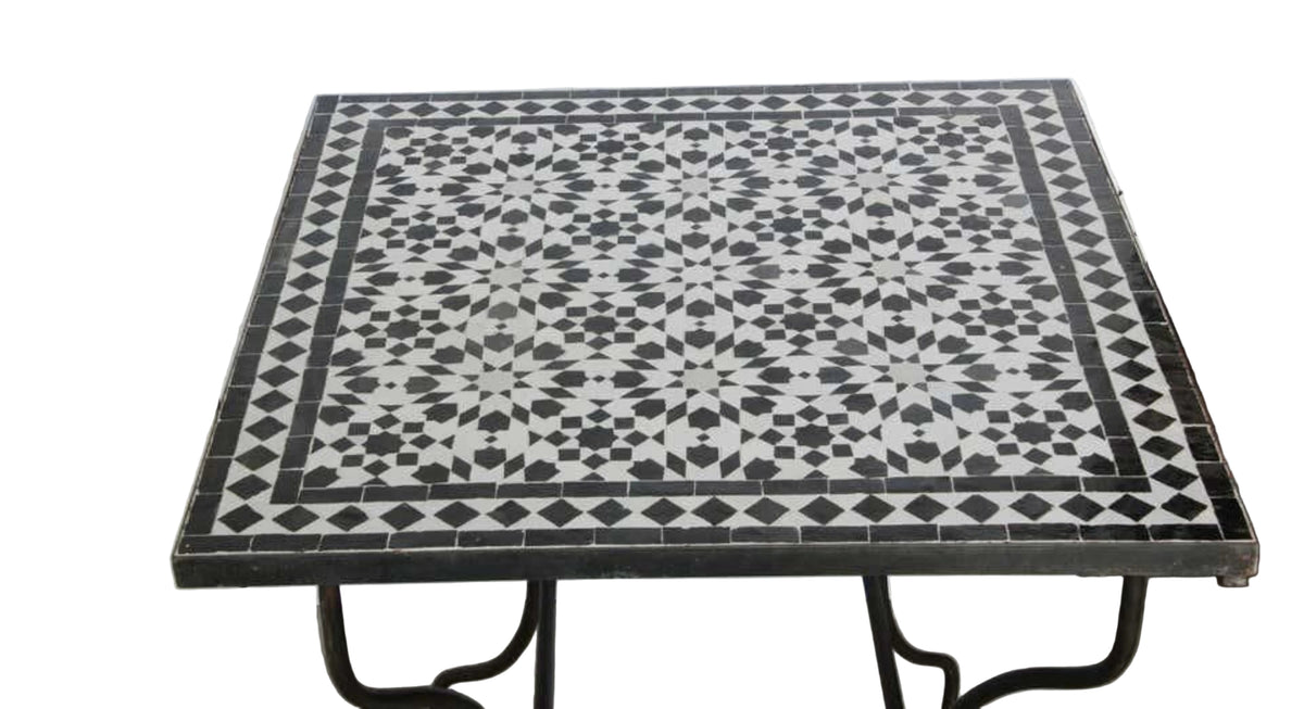 A square Moroccan table with a black and white geometric mosaic tile top and black metal legs, 