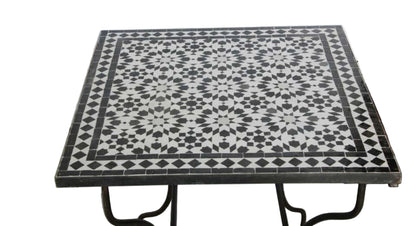 A square Moroccan table with a black and white geometric mosaic tile top and black metal legs, 