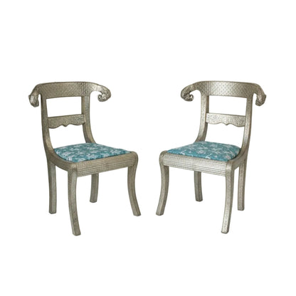 A pair of Anglo-Indian silvered wrapped clad side chairs with upholstered seats in blue and carved wooden legs, featuring intricate metalwork and elephant head designs. 