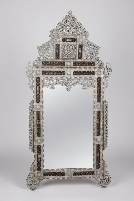 An ornate freestanding mirror with an intricate silver-toned filigree frame and dark brown inlay details, photographed against a neutral light gray background.